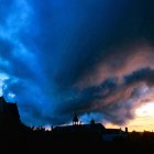 Surreal landscape painting: dramatic sky, wave-like clouds, countryside with castle ruin.