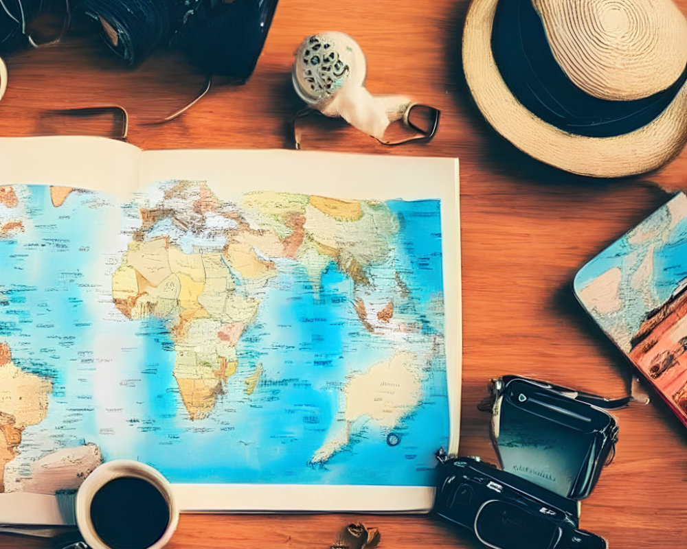 Open world map book on wooden table with coffee cup, vintage cameras, sunglasses, and straw hat for