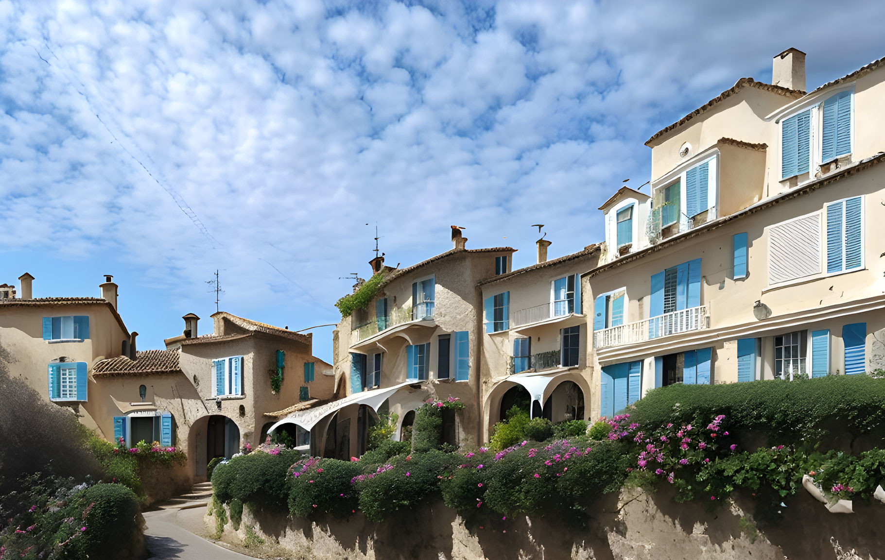 Picturesque European village street with traditional houses, shuttered windows, archways, and blooming flowers