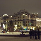 Snow-covered European town square at night with streetlights and church