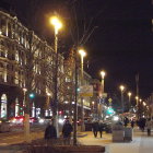 Snowy evening scene in historic town square with glowing street lamps and bustling activity