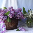 Wicker basket filled with purple and white flowers against white drapery and glass vase