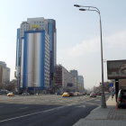 Colorful street scene with blue corner building, vintage cars, and pedestrians.