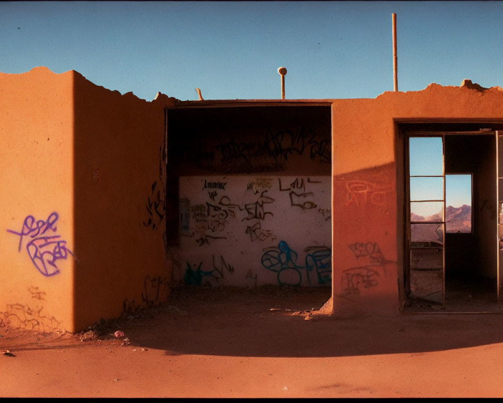 Abandoned structure with graffiti-covered walls and open doorways against mountain backdrop