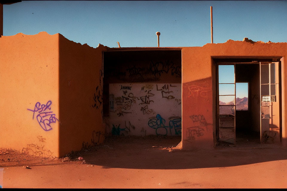 Abandoned structure with graffiti-covered walls and open doorways against mountain backdrop