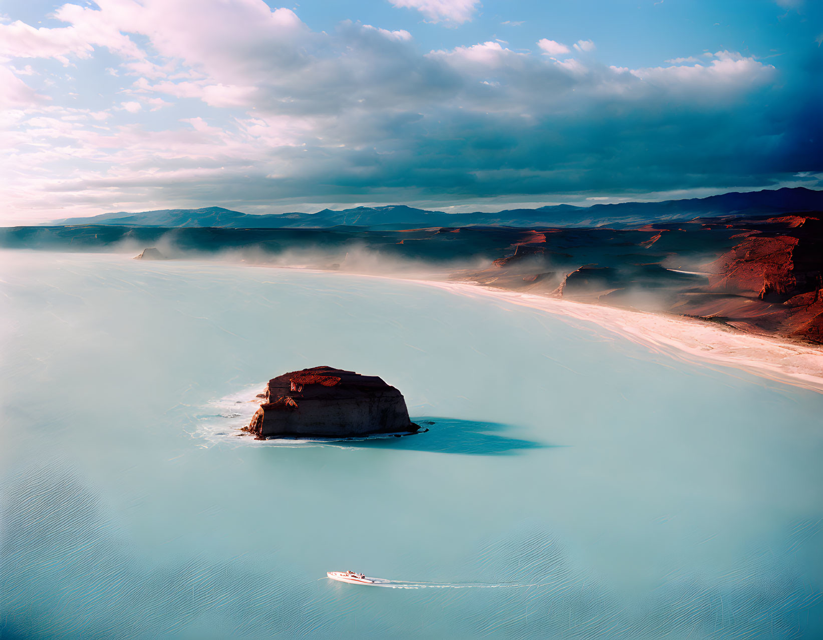 Tranquil landscape with blue water, rock formation, boat wake, and dramatic clouds