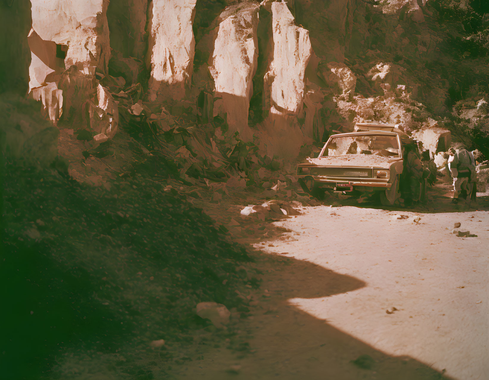 Abandoned car in rocky area under warm, reddish light