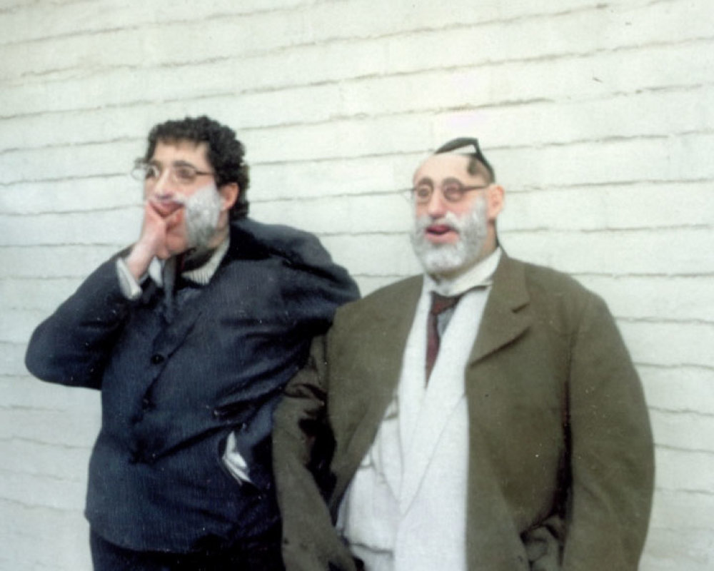 Two men posing with glasses and drawn mustaches on white brick wall