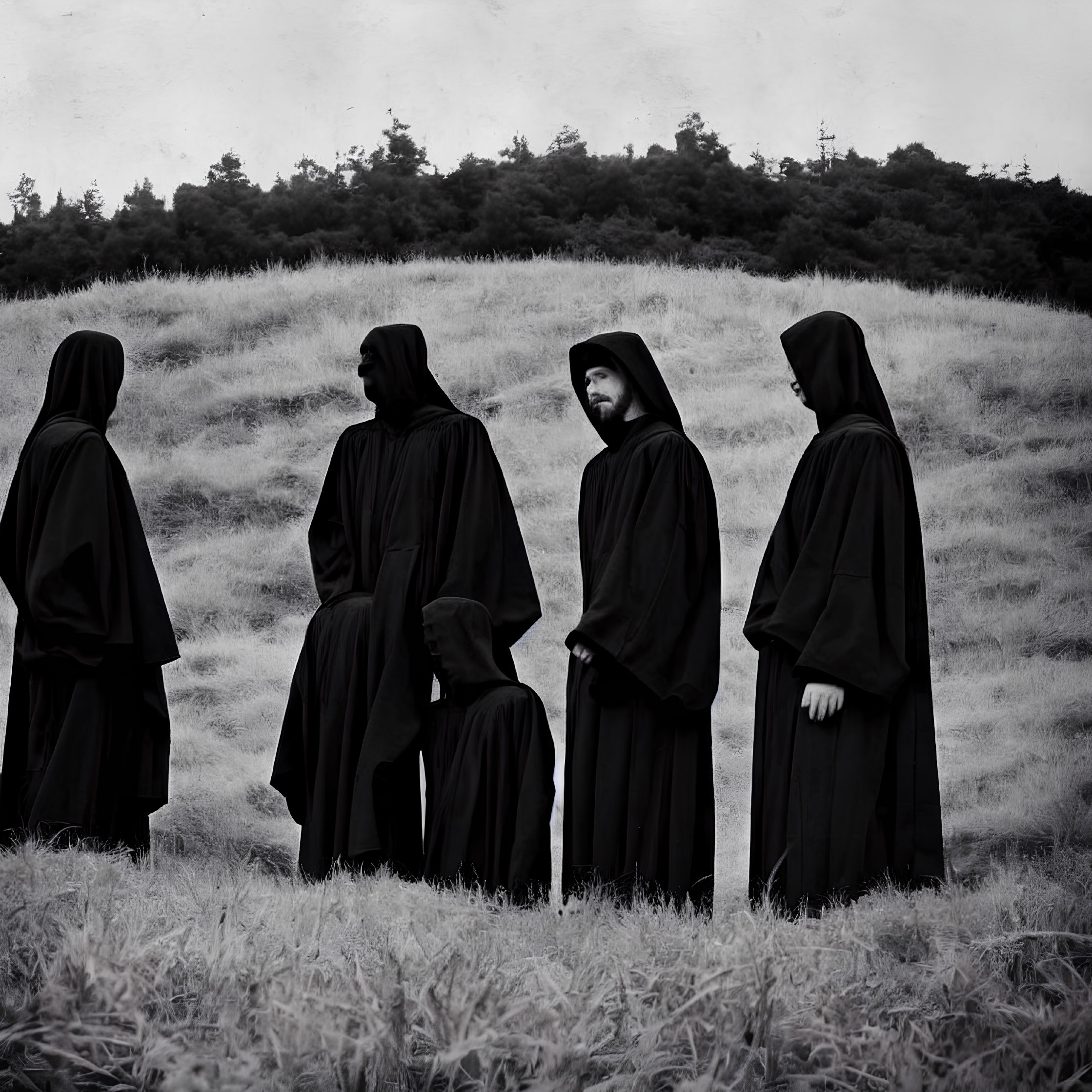 Four individuals in black cloaks in monochromatic field with forested hill