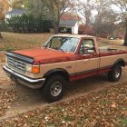 Vintage orange pickup truck in misty autumn forest with bare trees.