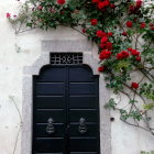 Ornate black iron door with gold details in white stone wall surrounded by red roses and green iv