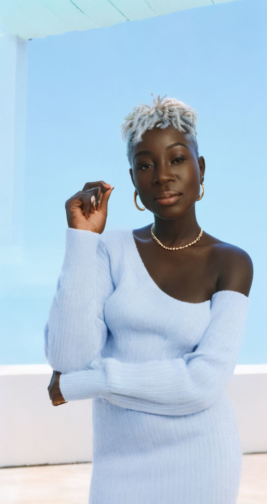 Short-haired woman in blue sweater and hoop earrings on blue-white backdrop