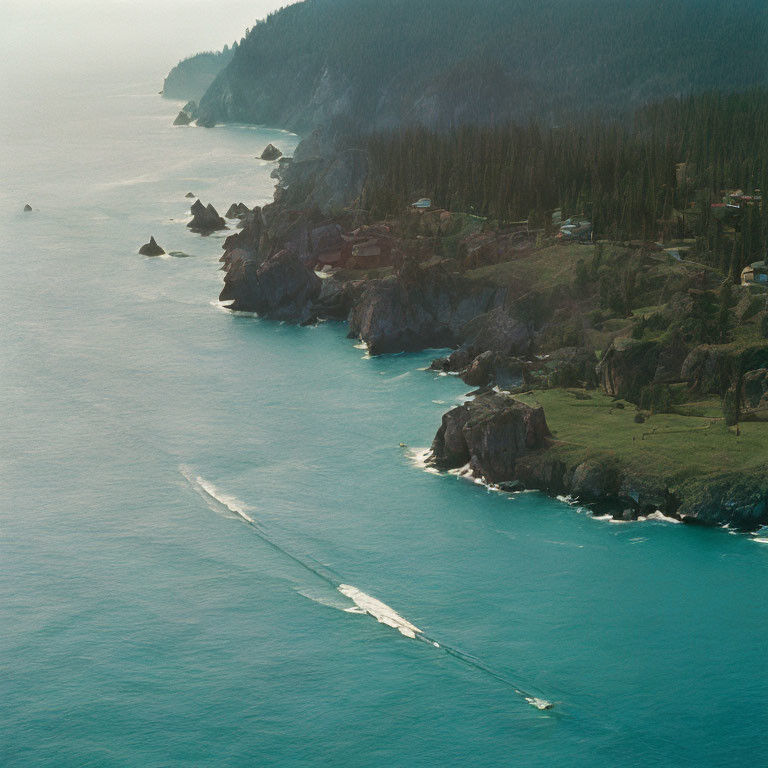 Rugged coastline with cliffs, pine trees, scattered buildings, and boat on turquoise sea