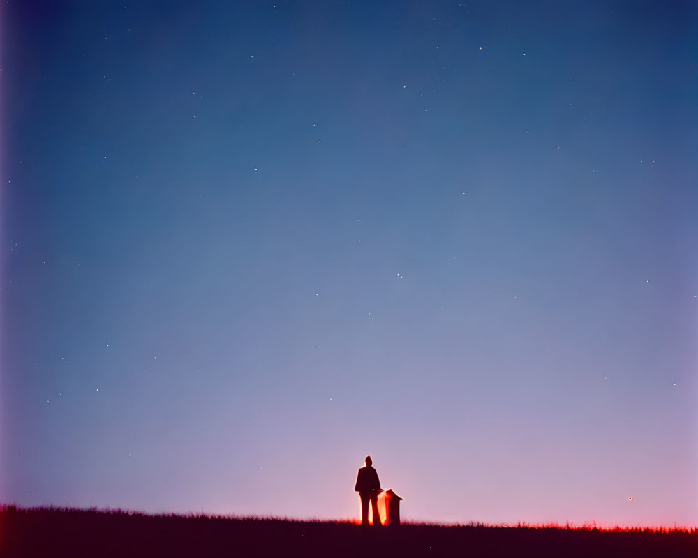 Solitary figure under starry twilight sky on hill