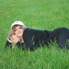 Woman in black outfit and white cap posing in green grassy field