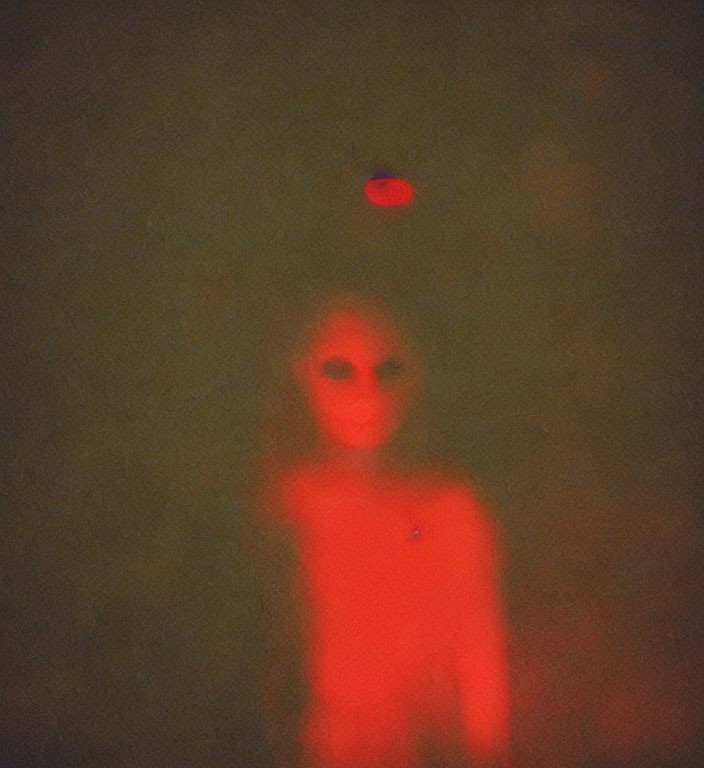 Blurred figure under red light in dim, grainy setting