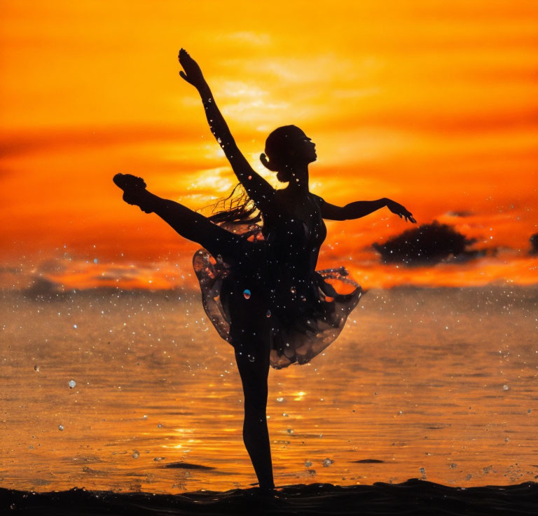 Silhouetted ballet dancer on beach at sunset with water droplets in elegant pose