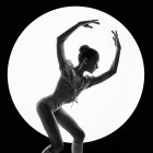 Graceful female figure dancer in glittery costume against luminous round backdrop