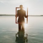 Person holding frame in water with sunlight and floating leaves