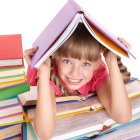 Young girl surrounded by colorful books with open book on head