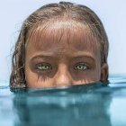 Surreal partial humanoid face with blue eyes in water with reflection and coral textures