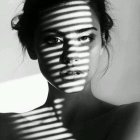 Monochrome portrait of a woman with striped shadow patterns, intense expression