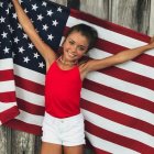 Young girl in patriotic outfit with sparkler, fireworks, and American flag scene.