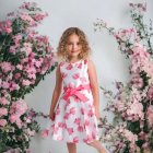 Young girl in floral dress surrounded by oversized flowers and wearing blooms in her hair