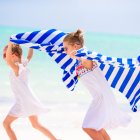 Children playing with a blanket on the beach with kites in the background