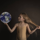 Porcelain-like figure with flowing hair and crown holding glowing Earth on dark background