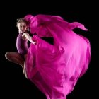 Elegant woman in flowing pink dress dances against colorful background