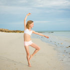 Surreal painting of young woman dancing on water with cloudy sky and rocks.