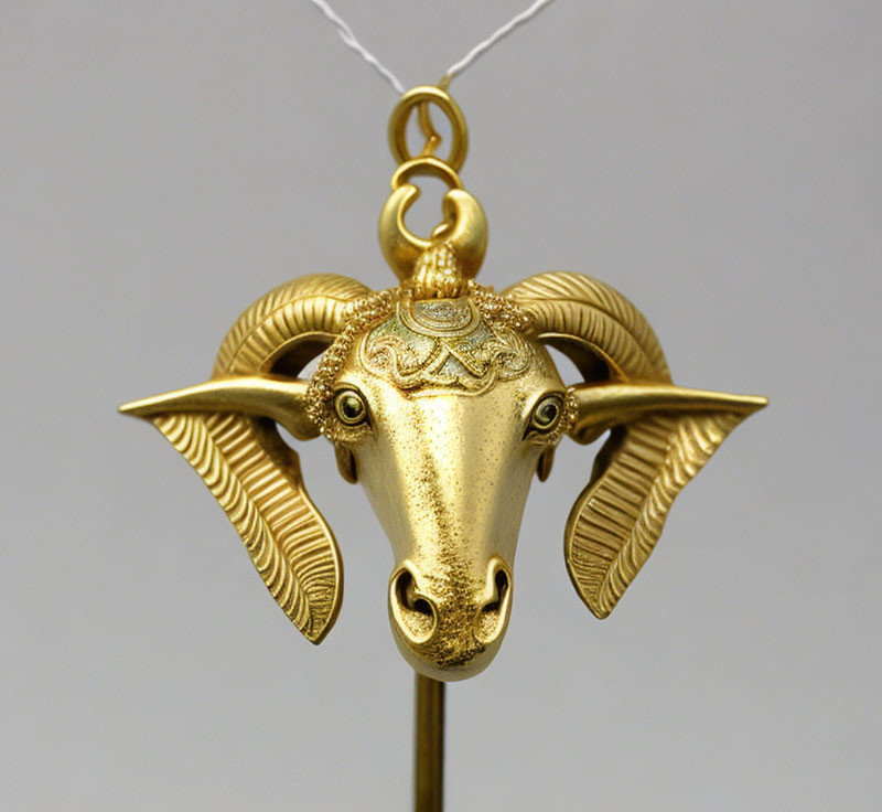 Intricately designed gold ram head pendant on chain against neutral backdrop