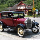 Vintage Red and Black Car with Yellow Spoked Wheels in Front of House