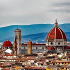 Iconic red dome of Florence cathedral among historic buildings and vibrant flowers under a hazy blue sky