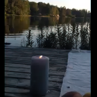 Calm lake scene: two candles in glass holders, dusk ambiance, greenery, forest backdrop