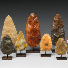 Seven polished gemstone sculptures in dark brown to orange colors on gray background