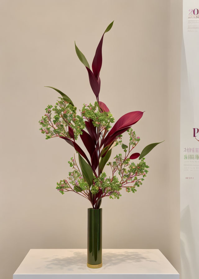 Floral arrangement with greenery and burgundy leaves in tall green vase