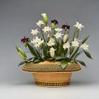 White lilies and green leaves in a basket on gray background