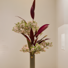 Floral arrangement with greenery and burgundy leaves in tall green vase