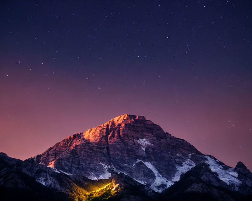 Mountain Peak Illuminated by Warm Glow Against Starry Night Sky