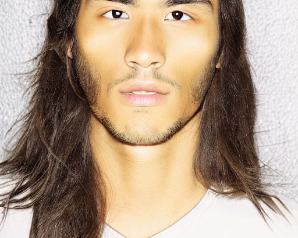 Portrait of man with long brown hair and light stubble in white shirt on grey background