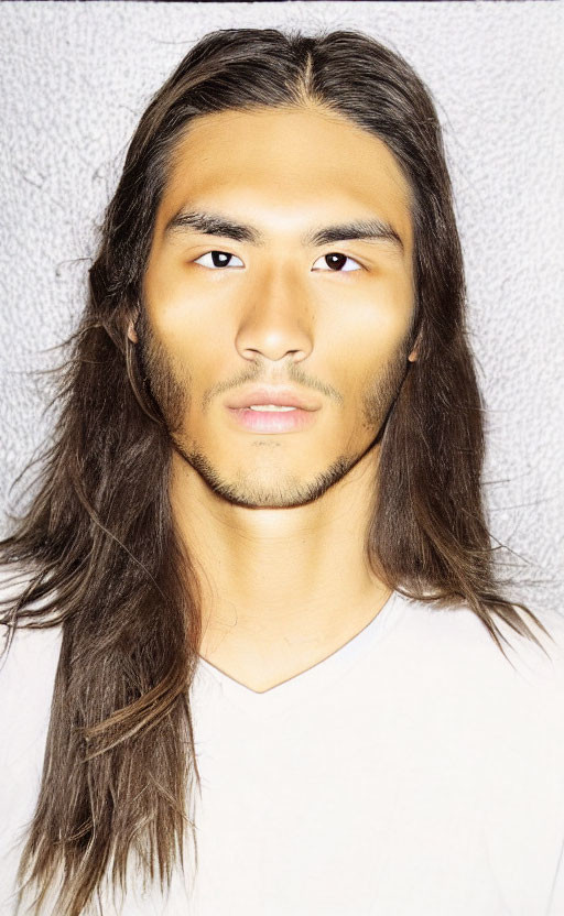 Portrait of man with long brown hair and light stubble in white shirt on grey background