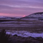 Snow-capped mountains under dusk sky with erupting peak in serene frozen landscape