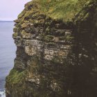 Cliffside scene with towering castle and secluded tower amidst lush greenery