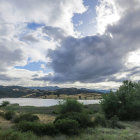 Scenic landscape: rolling green hills, dramatic sky, serene lake, cluster of trees