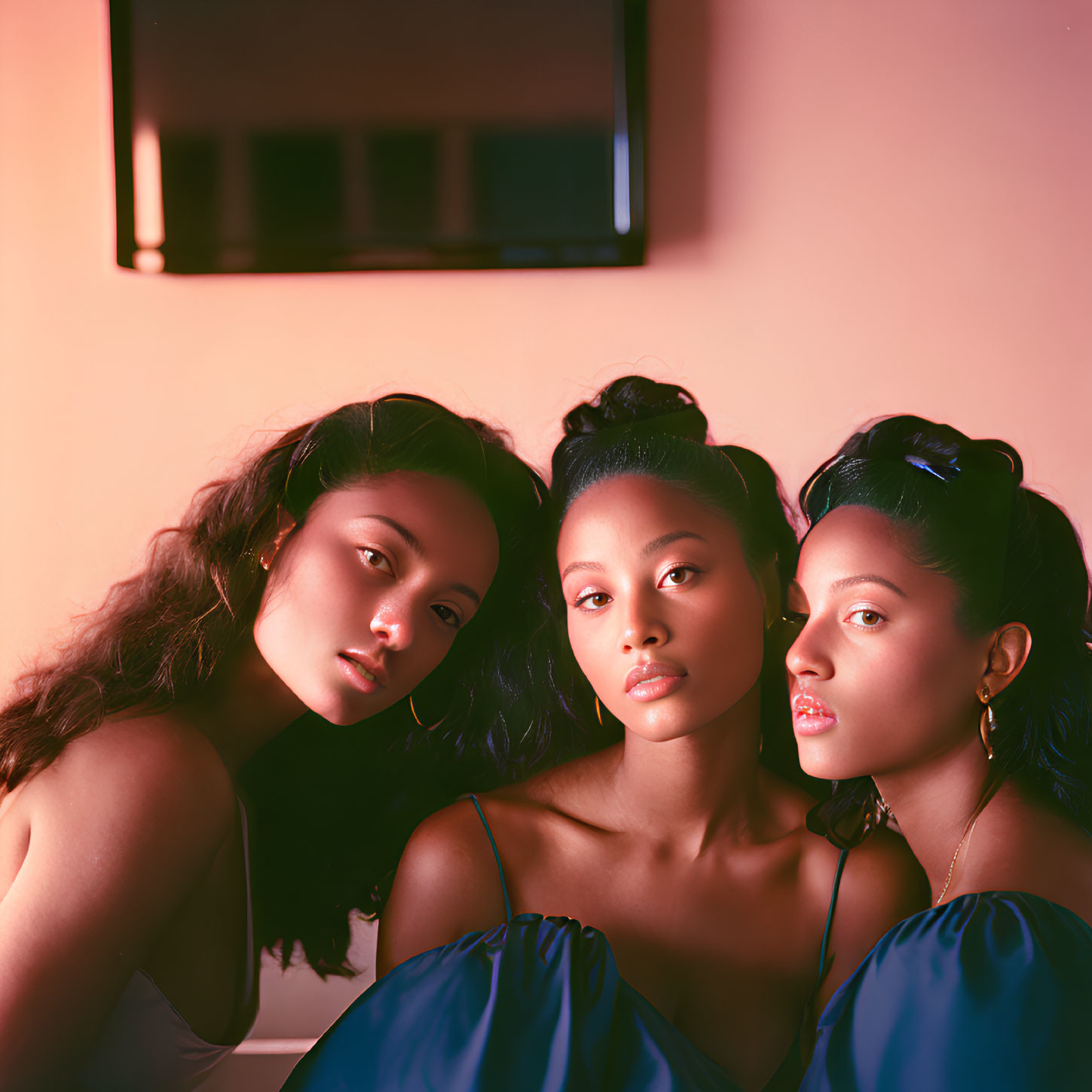 Three women in elegant blue dresses against warm-toned backdrop