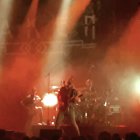 Silhouette of person on stage with raised arm in front of excited audience under red lights.