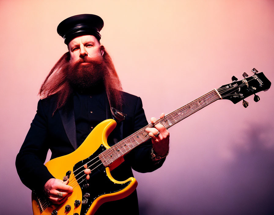 Long-bearded man in cap holding yellow electric guitar on pink background