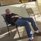 Elderly man relaxing in a rocking chair under dappled sunlight